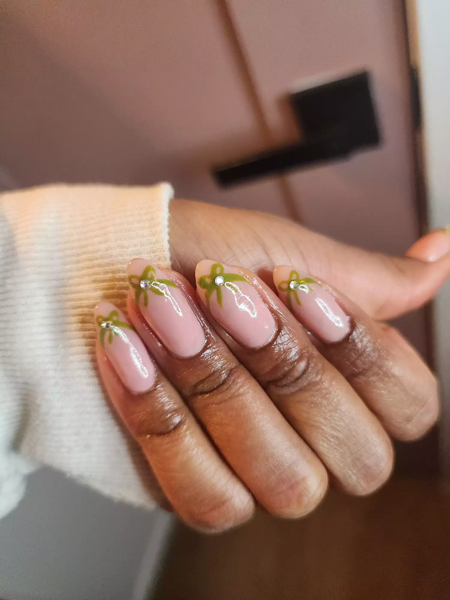 A hand with manicured nails decorated with small green bows and silver gems