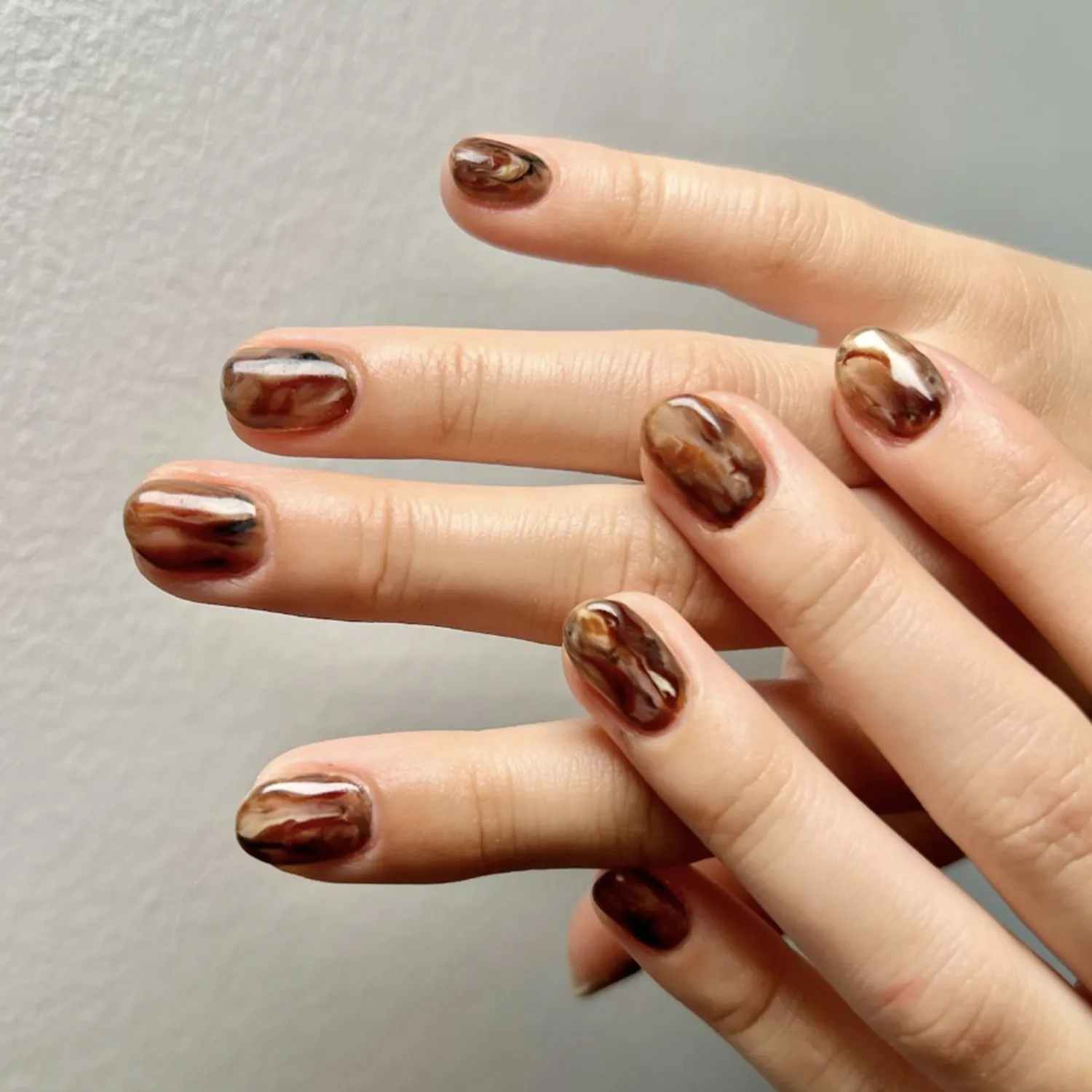 Hands displaying brown marbled nail designs on a soft background