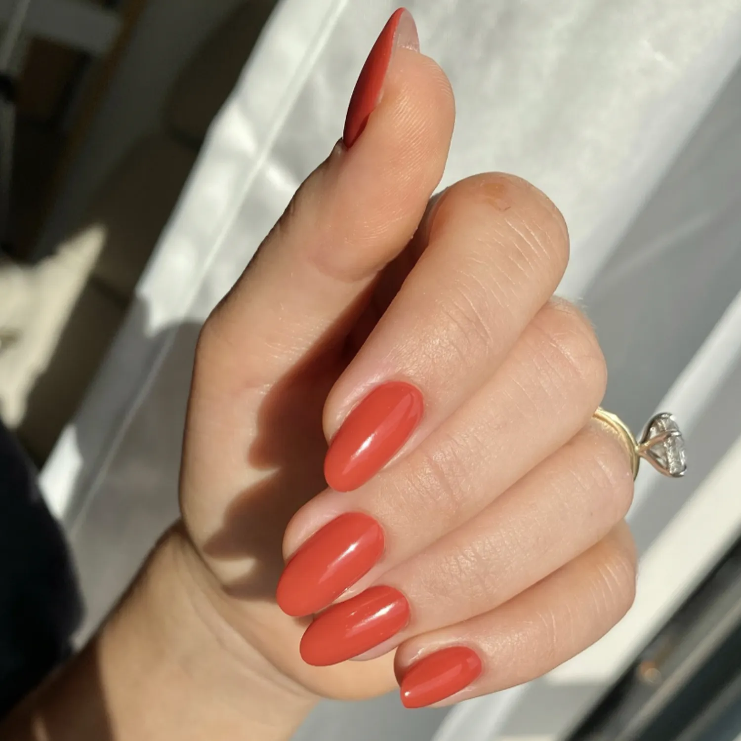 A hand with long almondshaped nails painted in a warm orange shade held in natural lighting with a ring visible on one finger