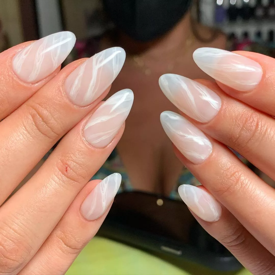 Person shows off their oval-shaped nails that are sheer white with a white marble pattern