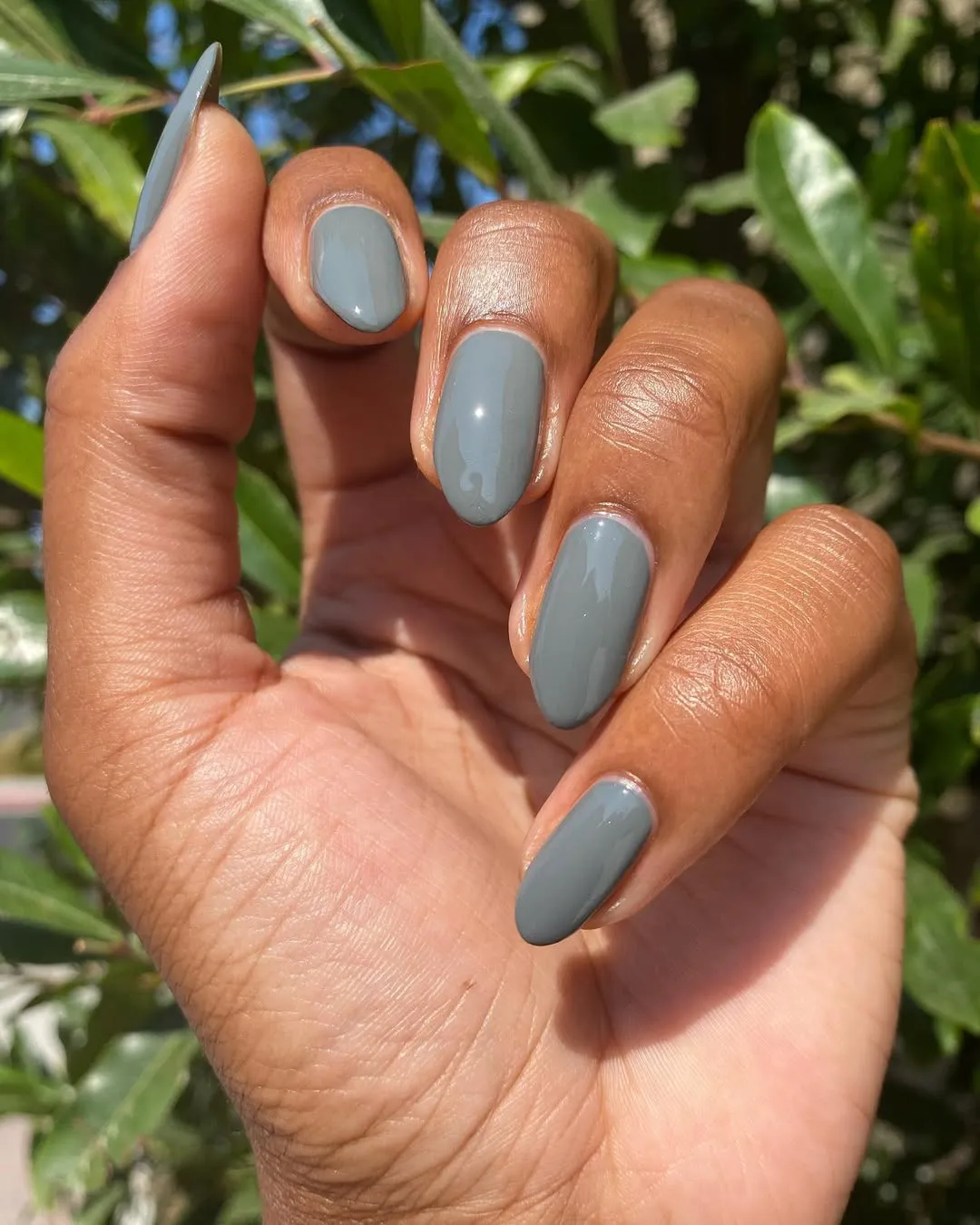 A hand with neatly manicured nails in a natural setting with plants in the background