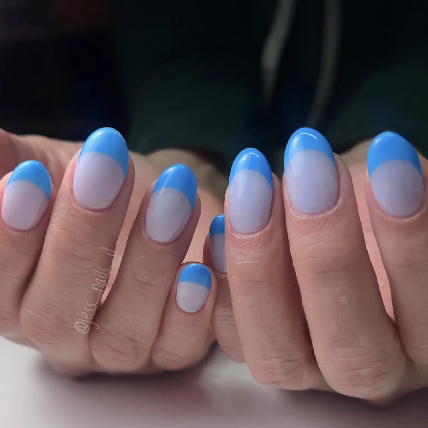 Hands with neatly manicured nails showing a gradient of light blue to white design