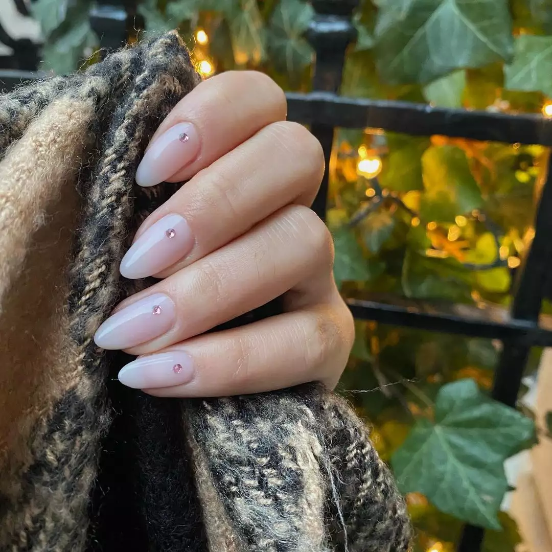 Hand with manicured gem nails holding fabric near a fence and foliage
