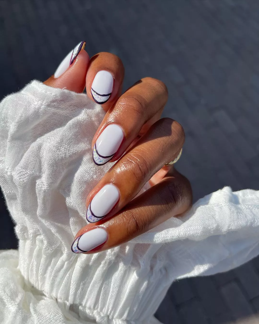 white manicure with added black outline and glitter tips