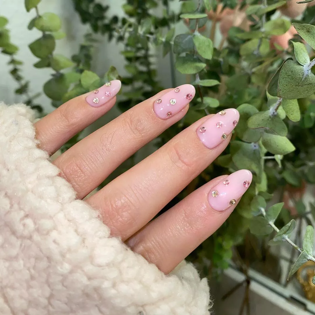 Hand with light pink gem nails surrounded by greenery