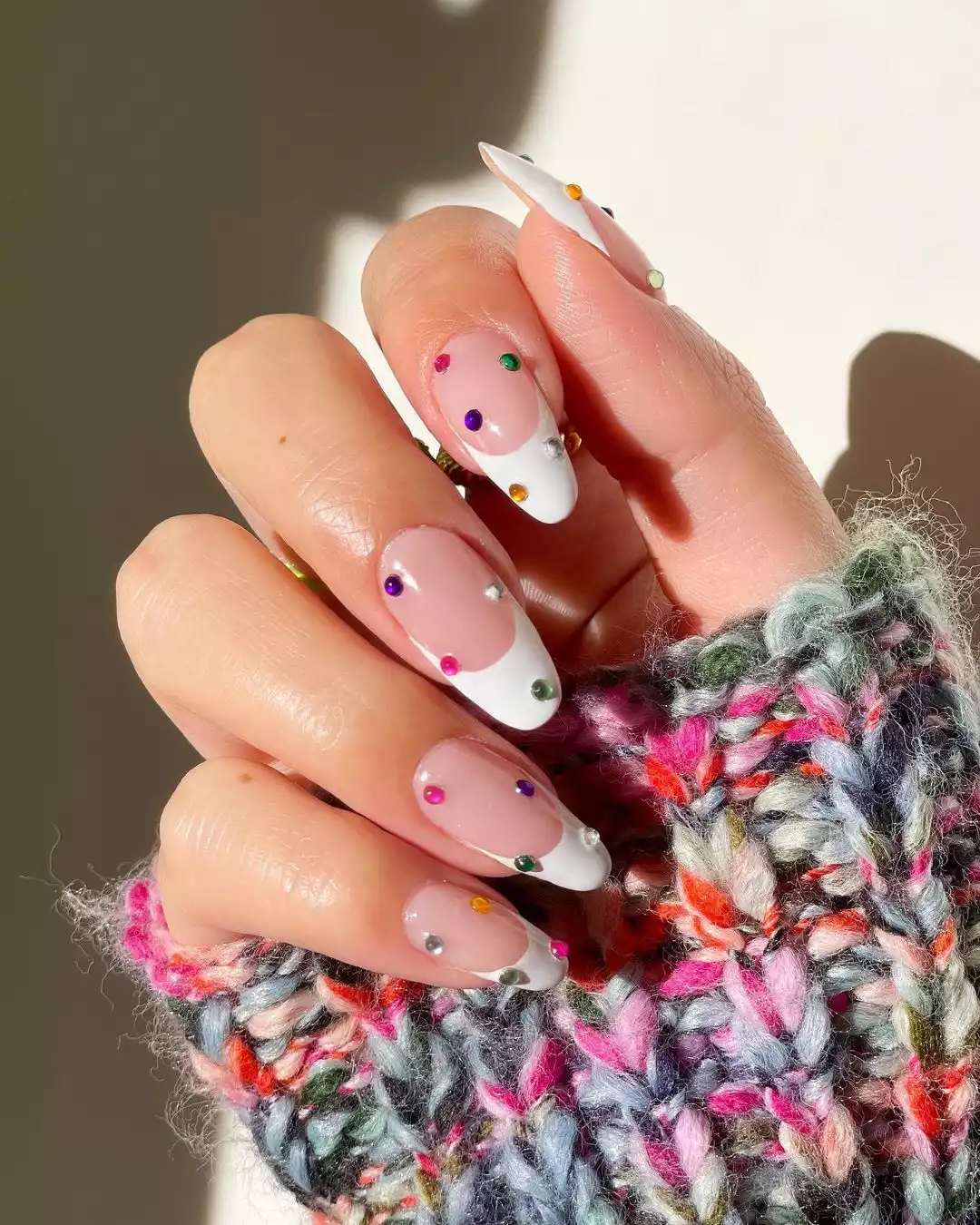 A hand with manicured nails featuring a white French tip design and colorful dot decorations