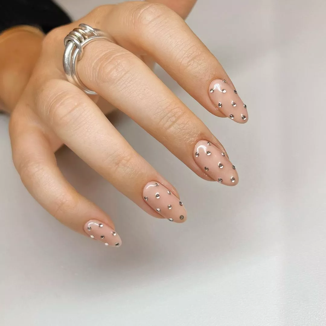 Hand with decorative nails featuring small designs and a ring on the finger