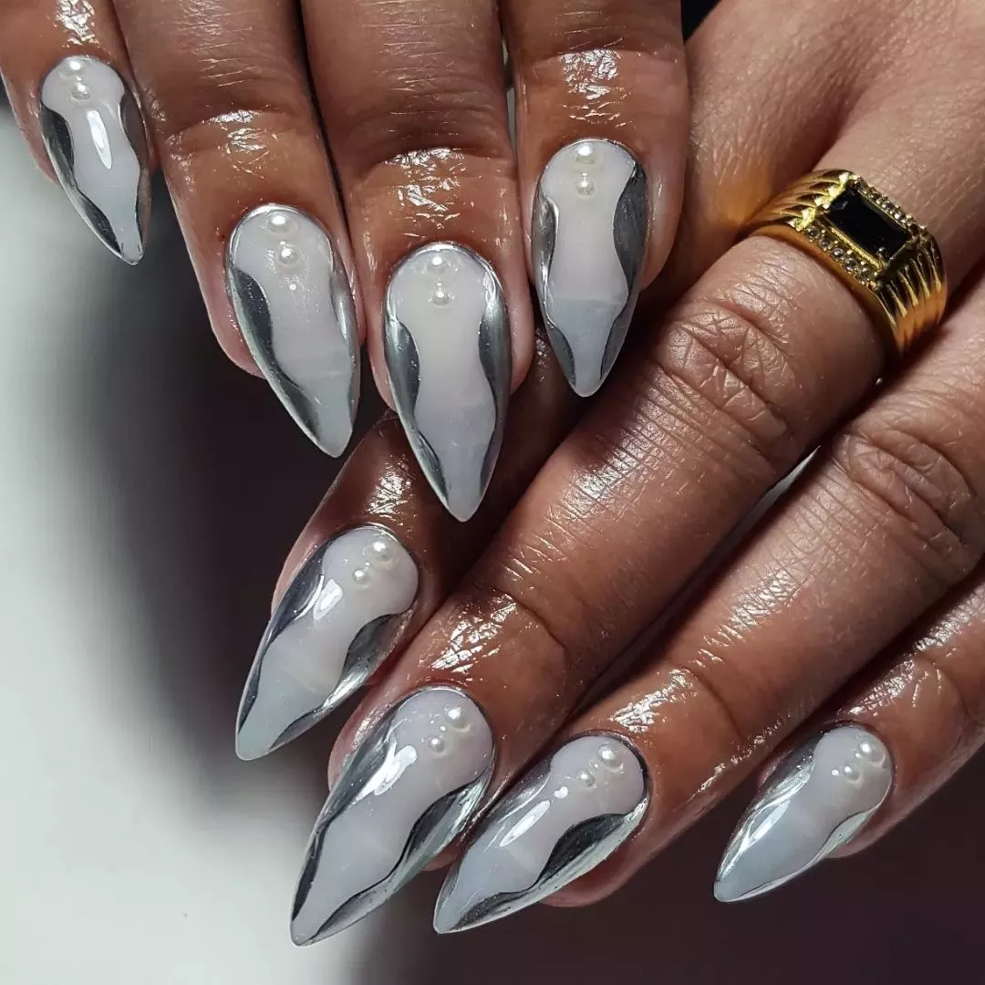 Closeup of hands with decorated pointed nails in an artful metallic design with pearl accents