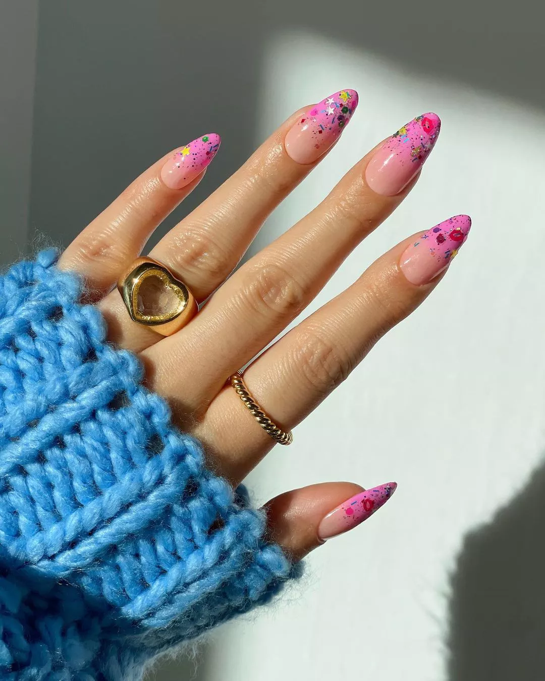 Person shows off their nails, which have pink French tips adorned with confetti