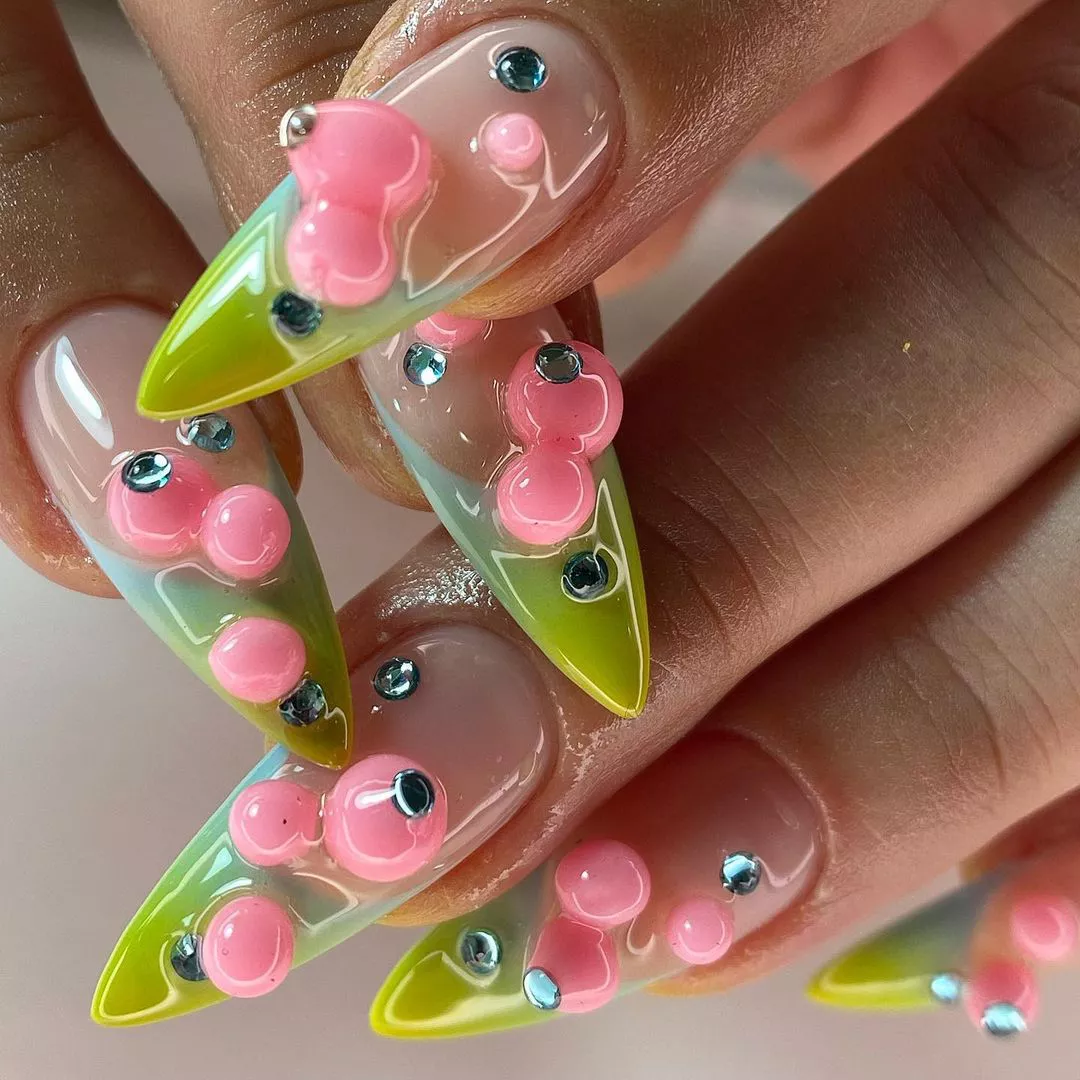 Closeup of hands with nails featuring green tips pink bubble-like designs and small rhinestones