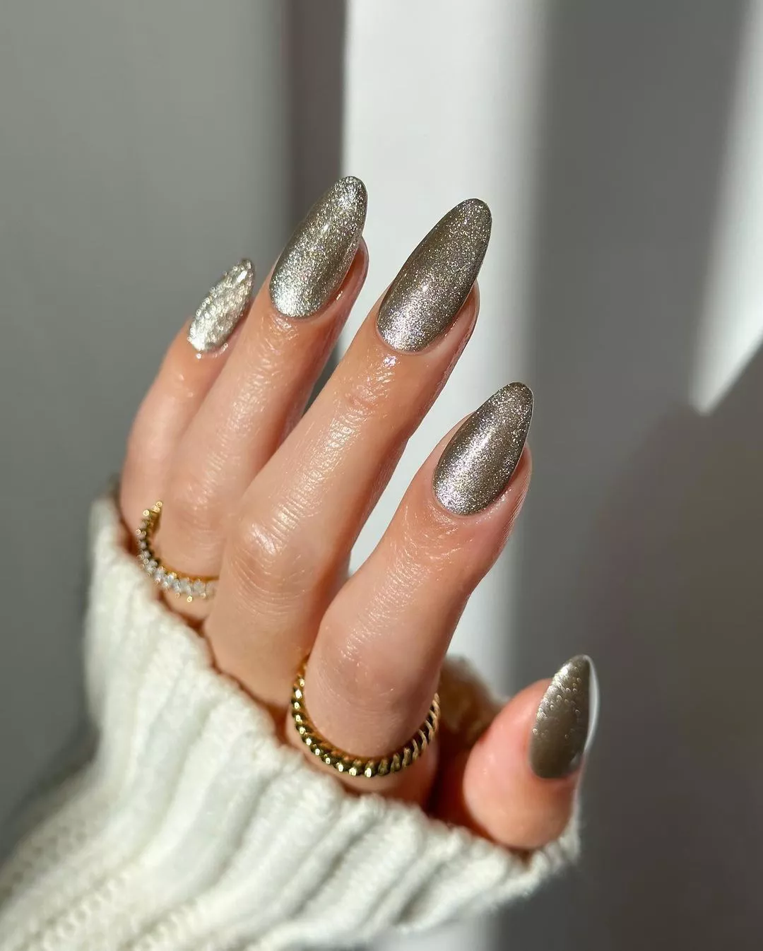 A hand with metallic polished nails rings on fingers and a ribbed sleeve visible