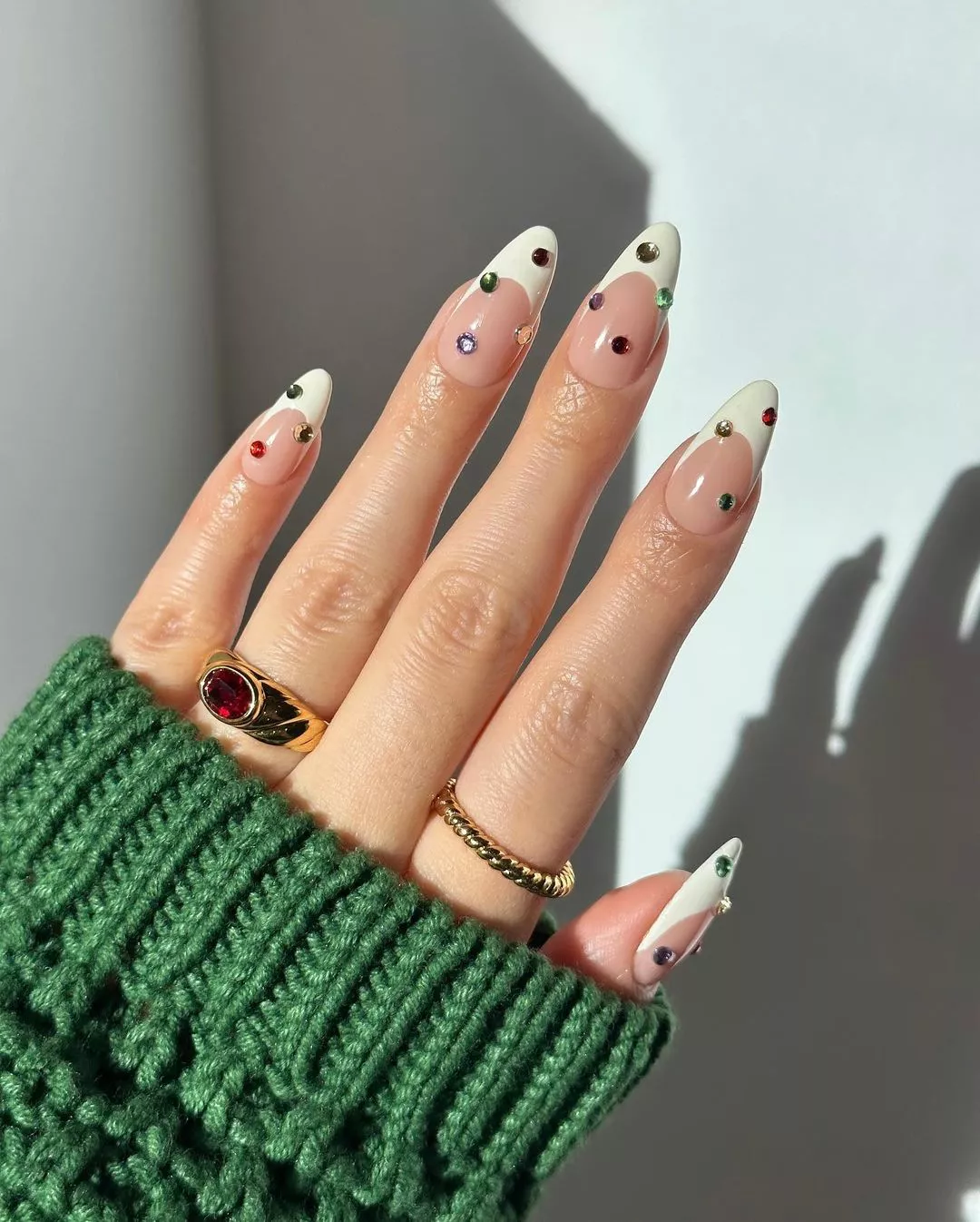 Person with an almond-shaped, French tip manicure that has colorful gems on each nail
