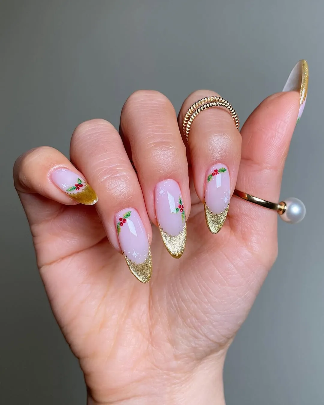A closeup of a hand with long nails painted with gold French tips and small floral designs adorned with rings