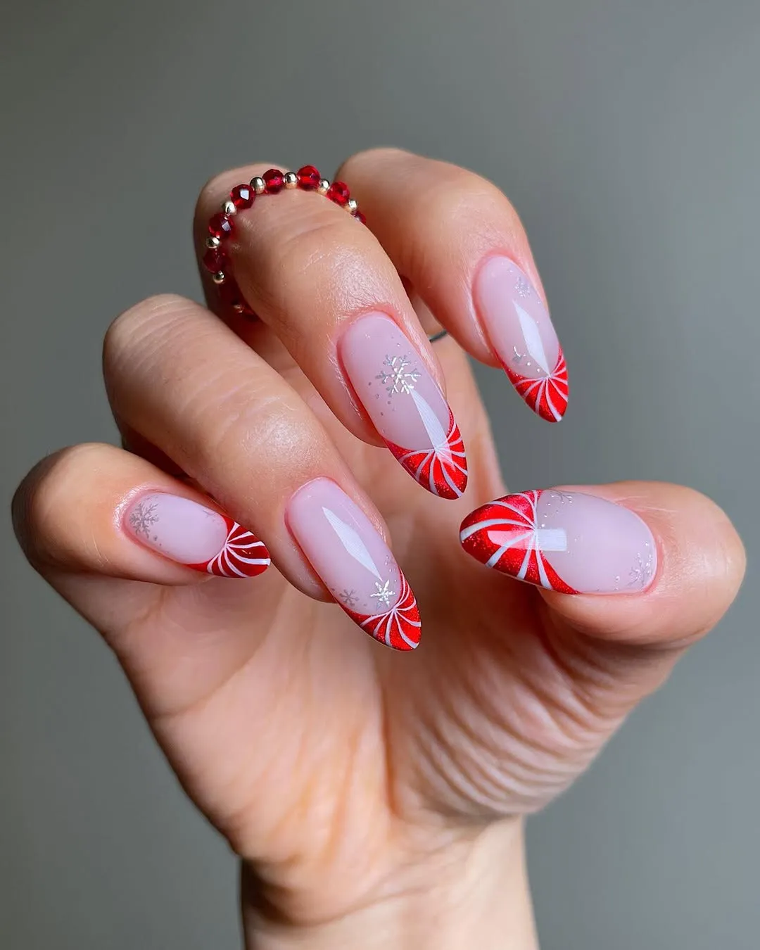 A hand wearing red and white nail art with a candy canethemed design on the nails