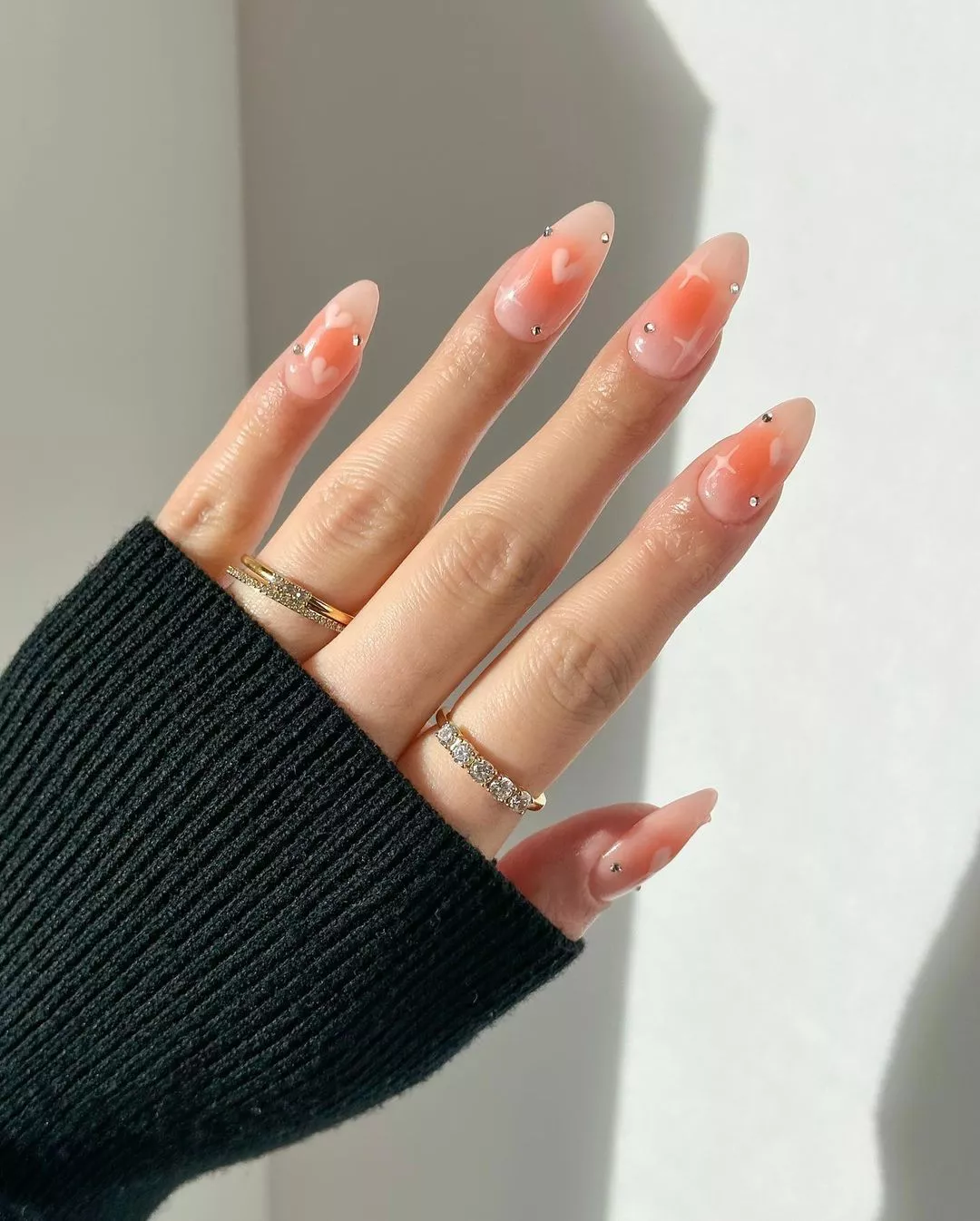 Person with light pink aura nails that are almond-shaped and studded with gems