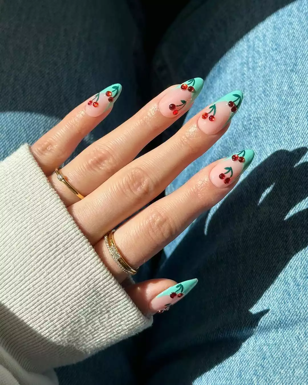Person with medium-length, almond-shaped nails that have red gems in the form of cherries