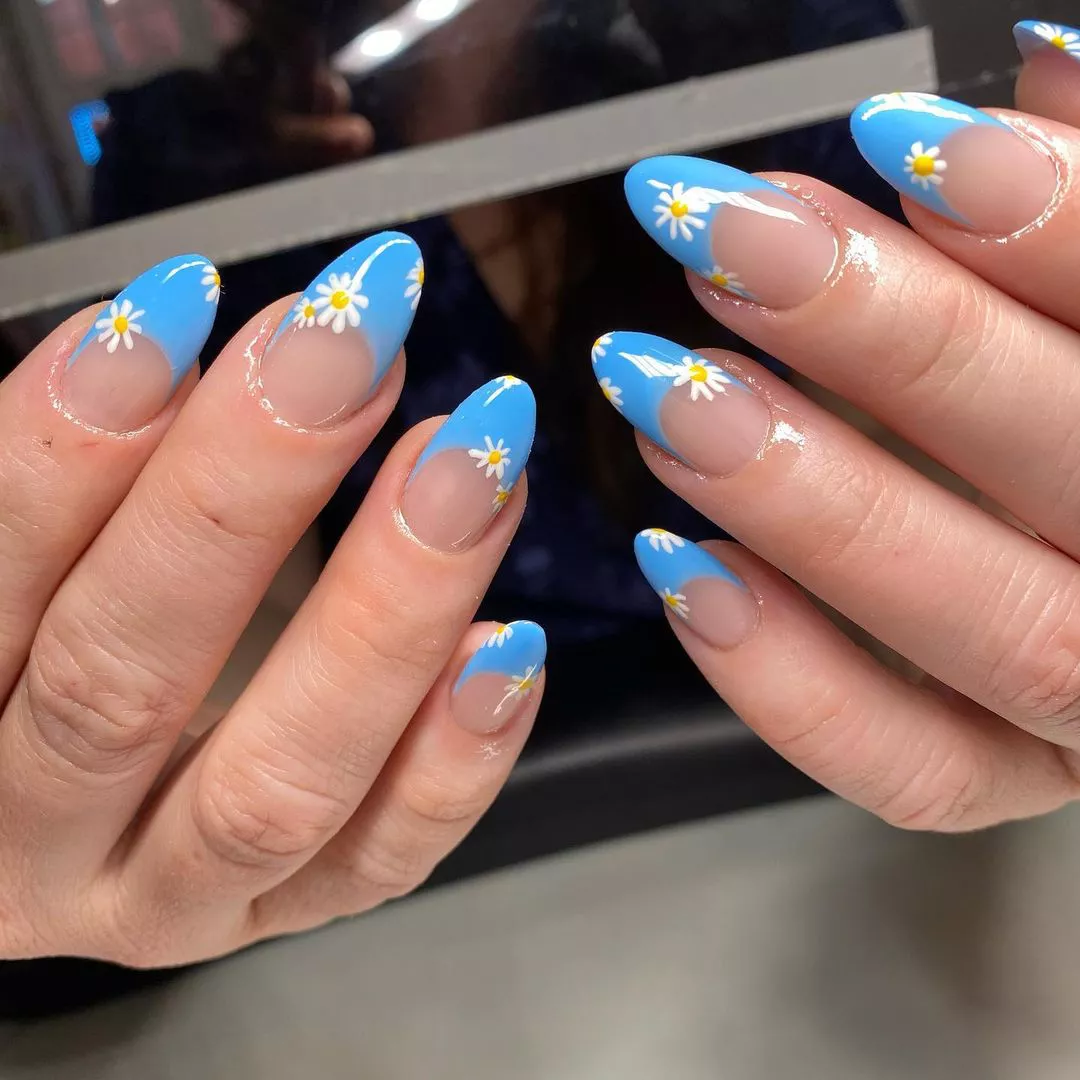 Person showing off their oval nails with sky blue French tips and hand-painted daisies