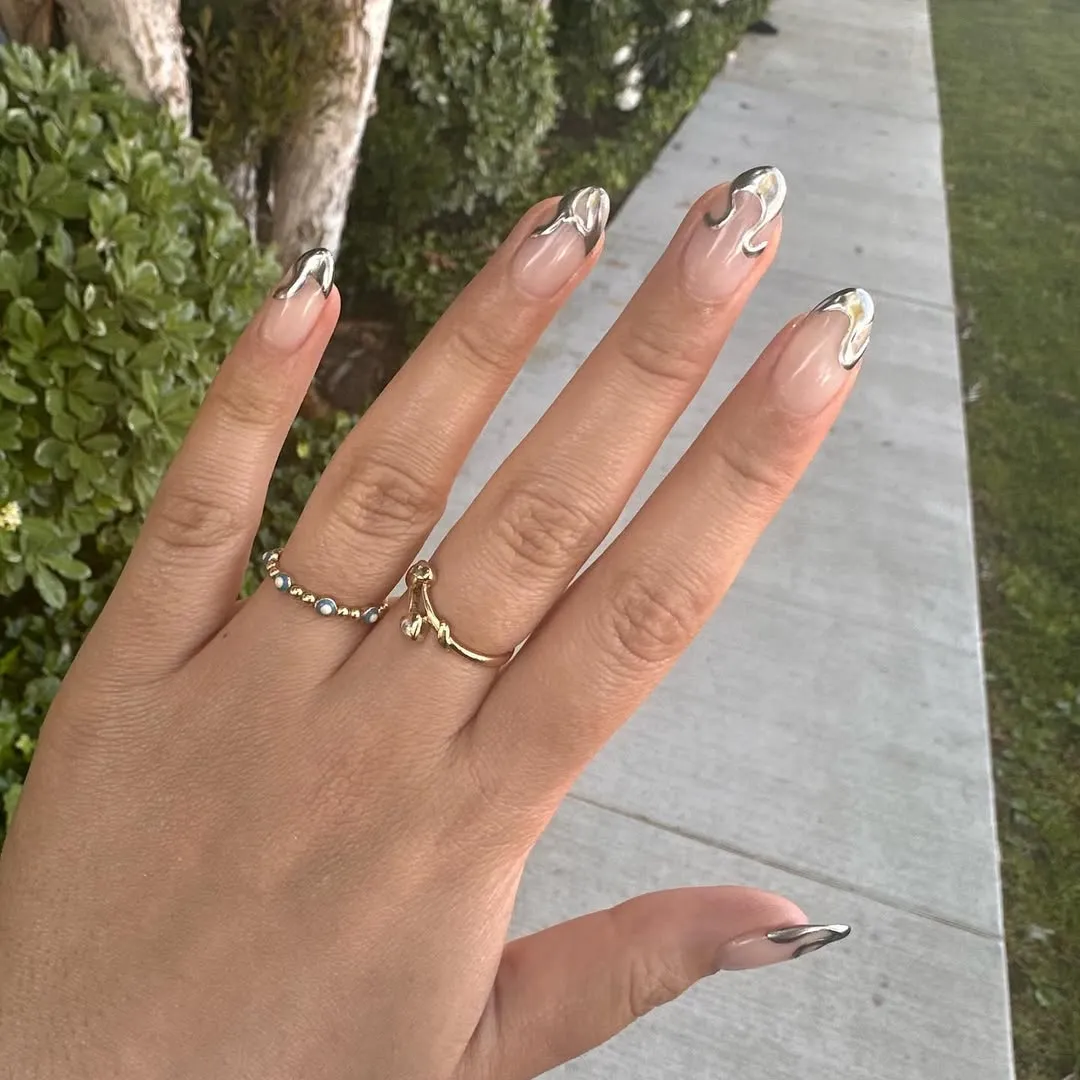 A hand with manicured nails featuring intricate designs wearing two rings