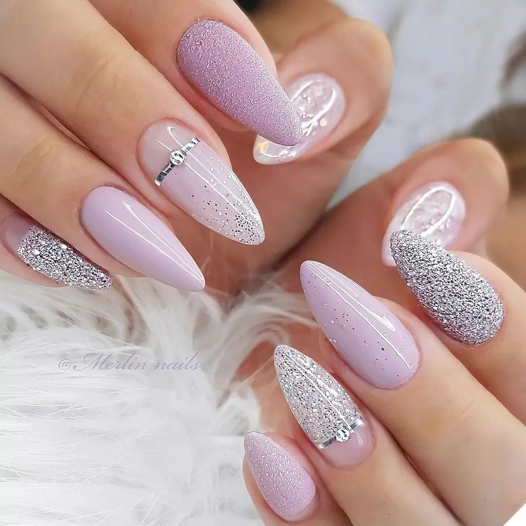 Person with lavender nails in a mix and match glittery pattern with ring accents