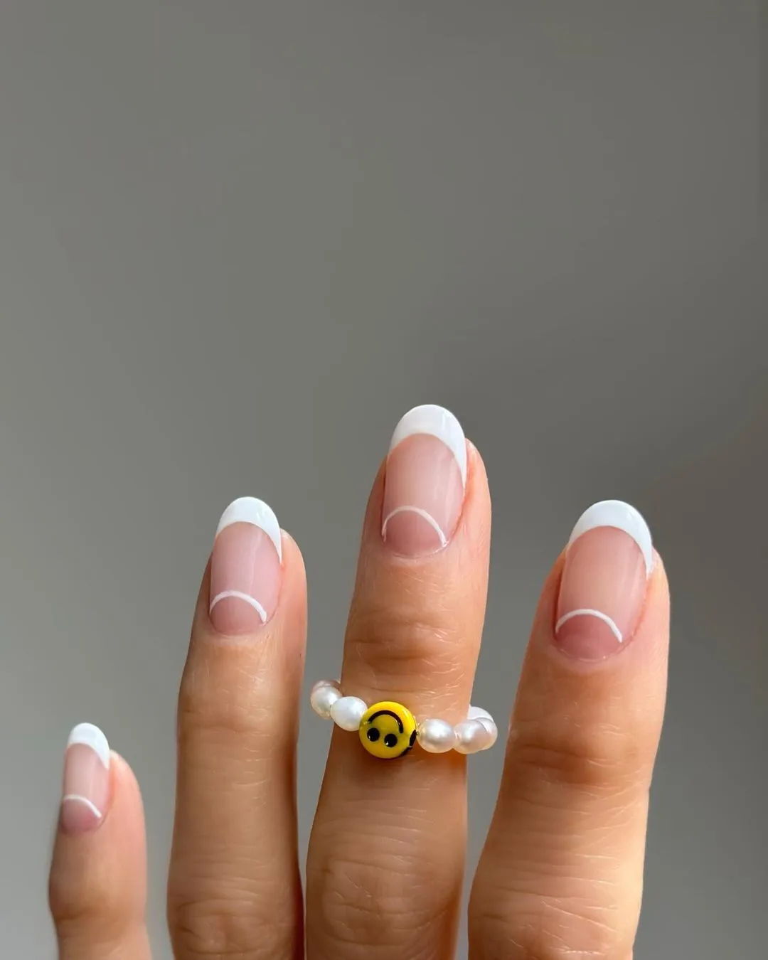 Person with oval-shaped nails that have white French tips and an arched white line at the base