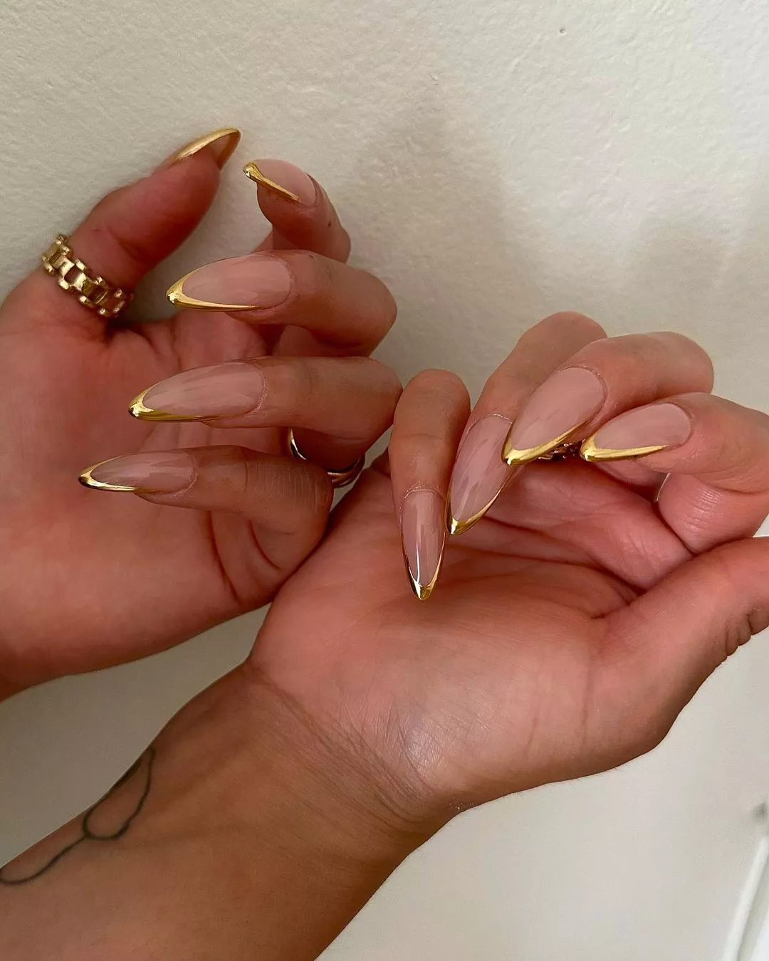 Person showing their stiletto-shaped nails that are outlined with gold French tips