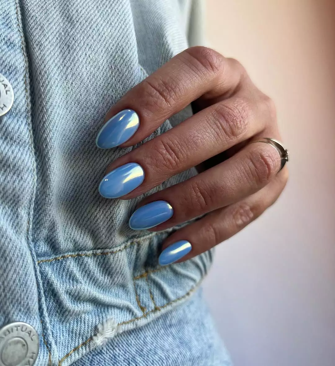 Person with baby blue chrome nails holds them against her denim jacket