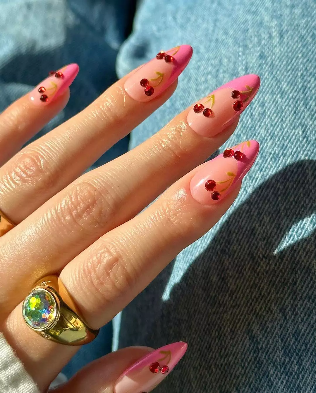 Medium-length, almond-shaped nails that have pink French tips and cherry gems