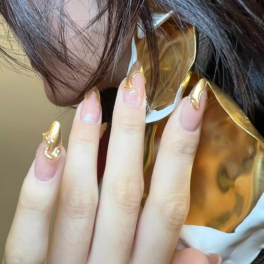 Person wearing artistic gold painted nails and highlighting a reflective accessory