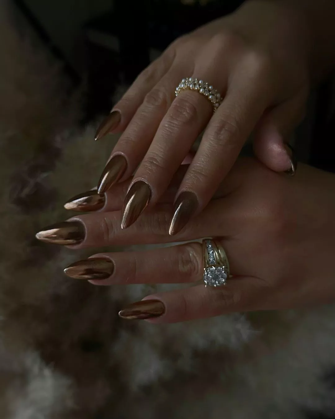 Hands with decorative rings and long metallic nails against a furry background