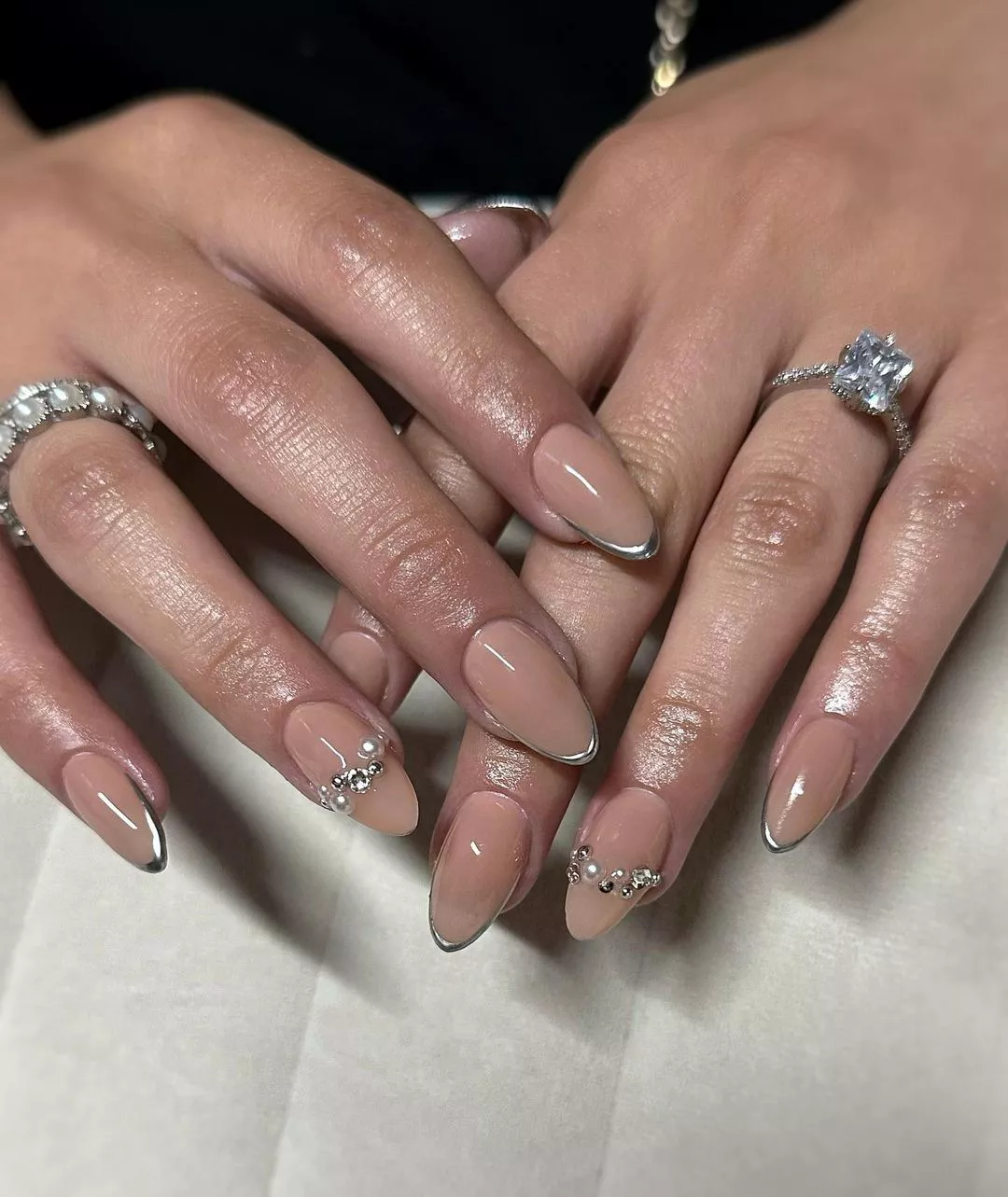 Manicured hands with decorative rings and gel nails featuring metallic tips and gemstone accents