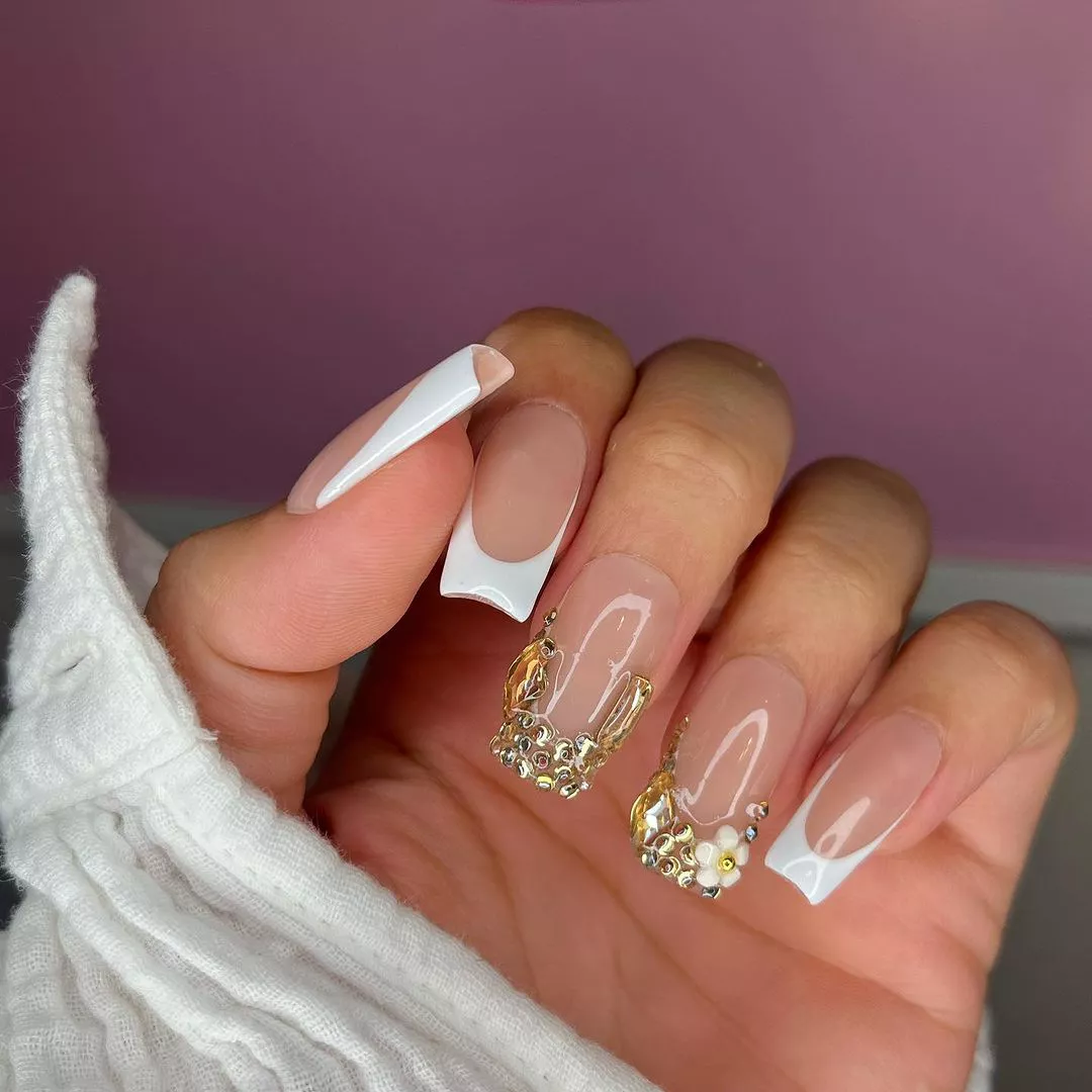 A hand with long manicured nails decorated with white tips and intricate gems on two fingers