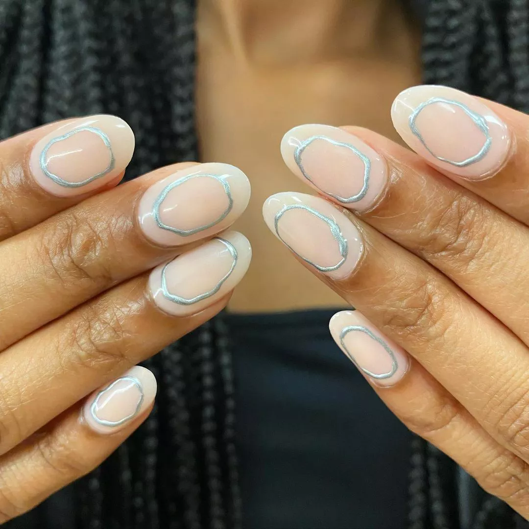 Closeup of hands showcasing nails with metallic circles and a braided hairstyle in the background