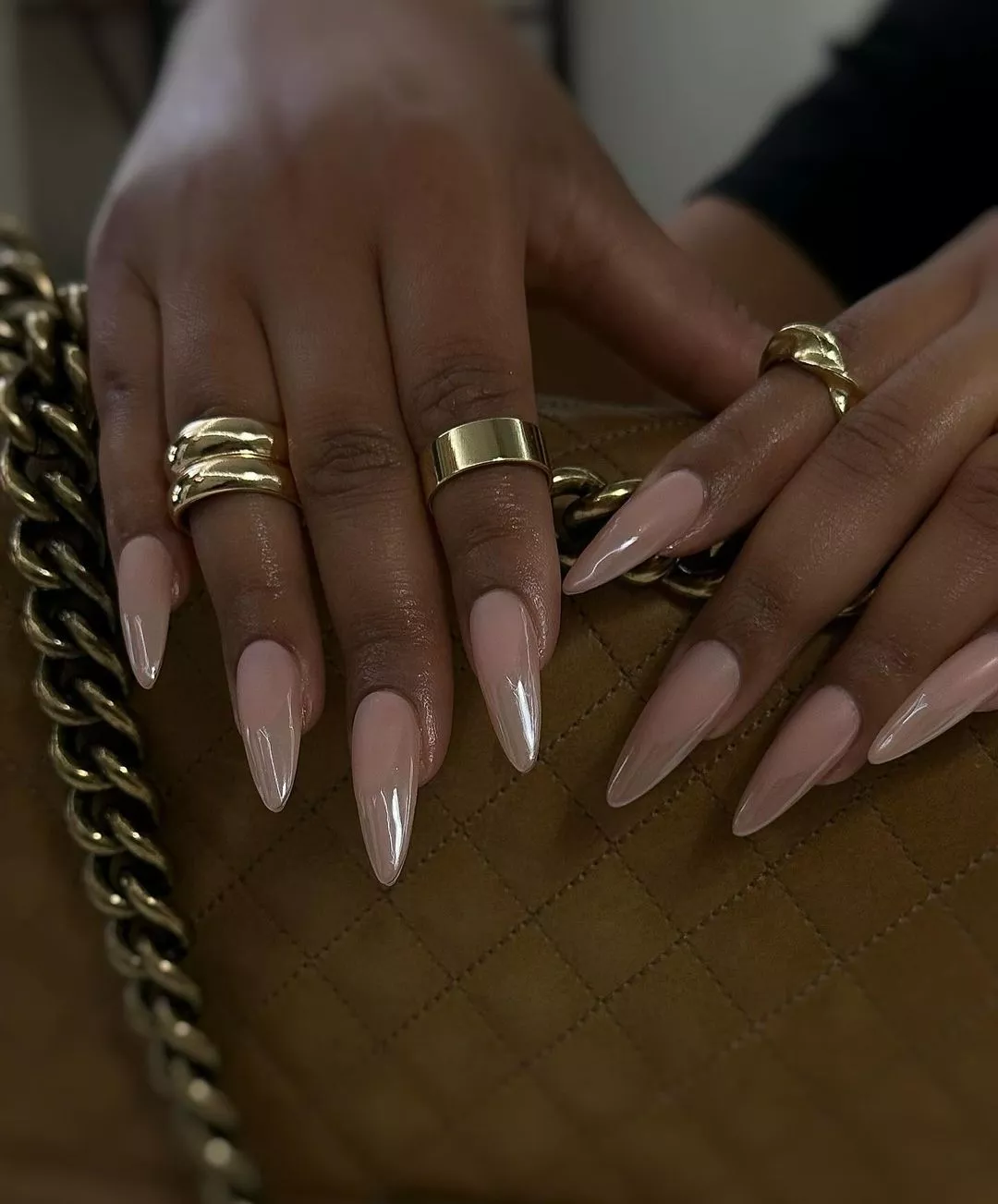 Hands with long manicured nails and gold jewelry holding a quilted handbag with a chain strap