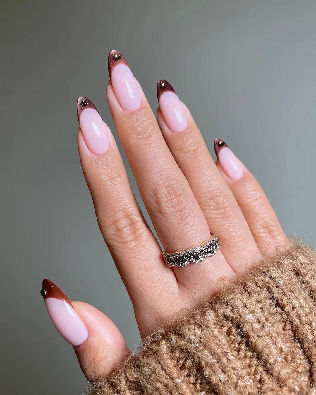 A hand displaying manicured nails with a decorative design wearing a ring and a sweater sleeve visible
