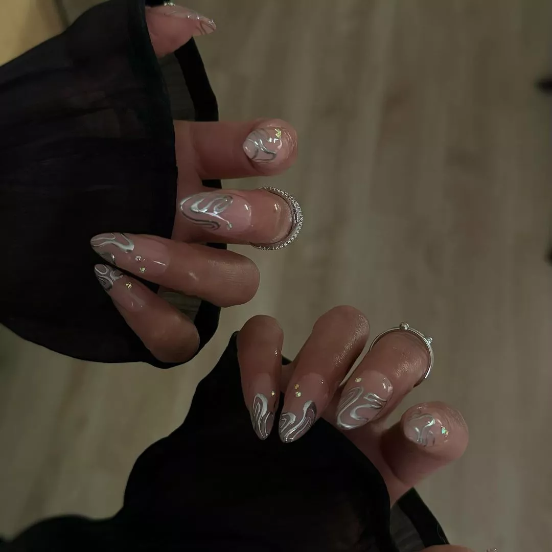 Person showing off their almond-shaped manicure, which have metallic accents on each nail