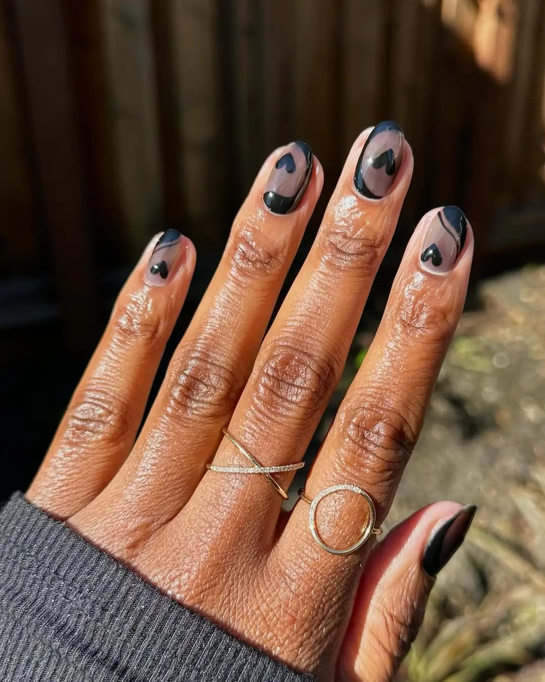 Person shows off their black and sheer gray manicure featuring hand-painted swirls and hearts