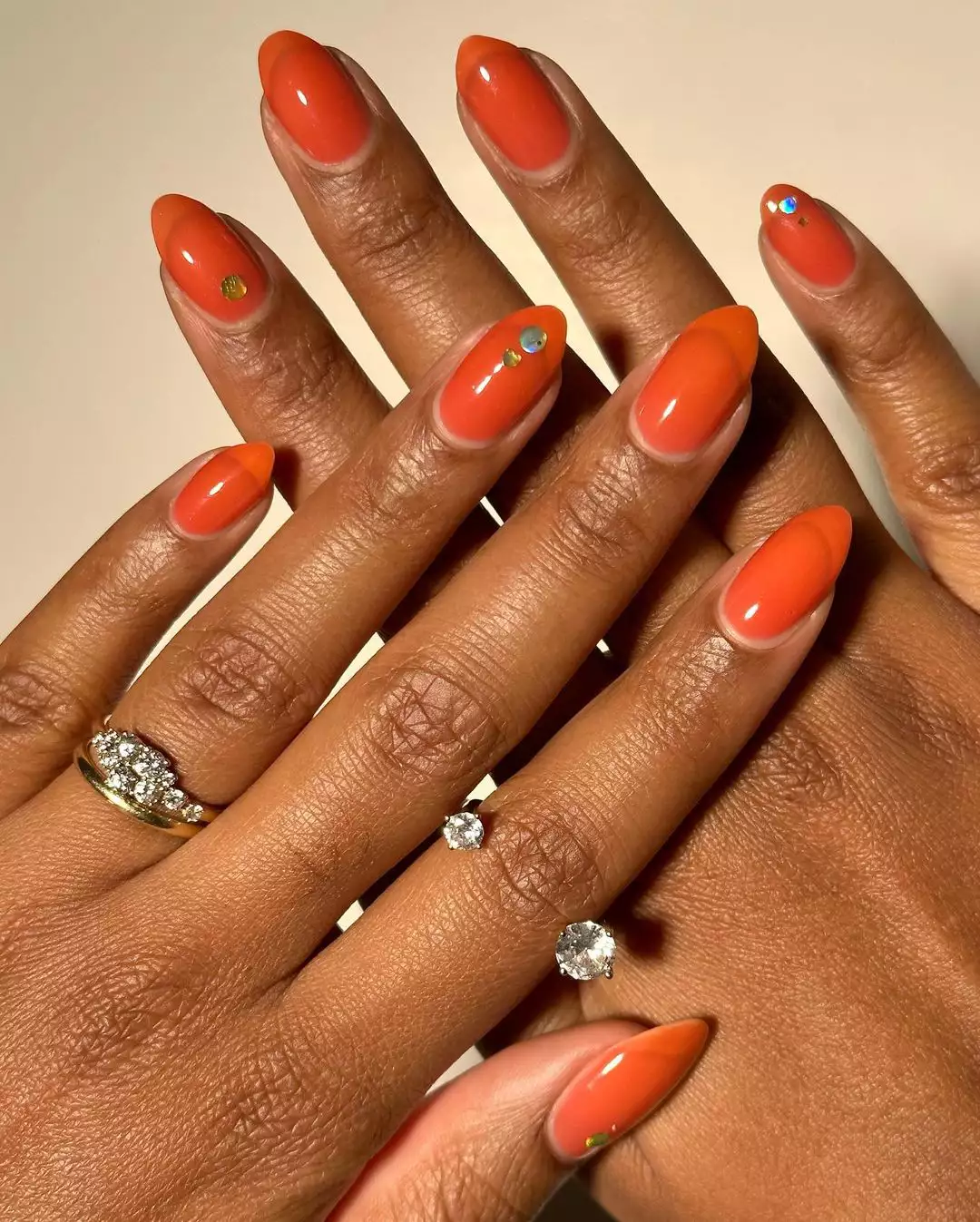Person with translucent orange nails in a short stiletto shape with silver sparkles on three nails