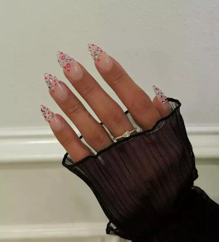 Person with stiletto-shaped nails that have pink and purple gems at the tips