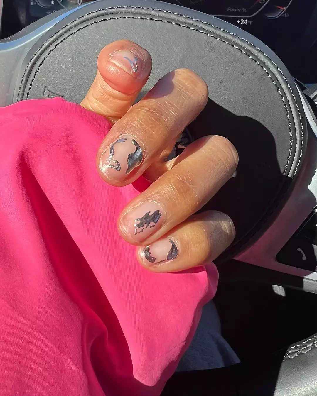 A hand displaying intricate metallic nail art against a steering wheel background