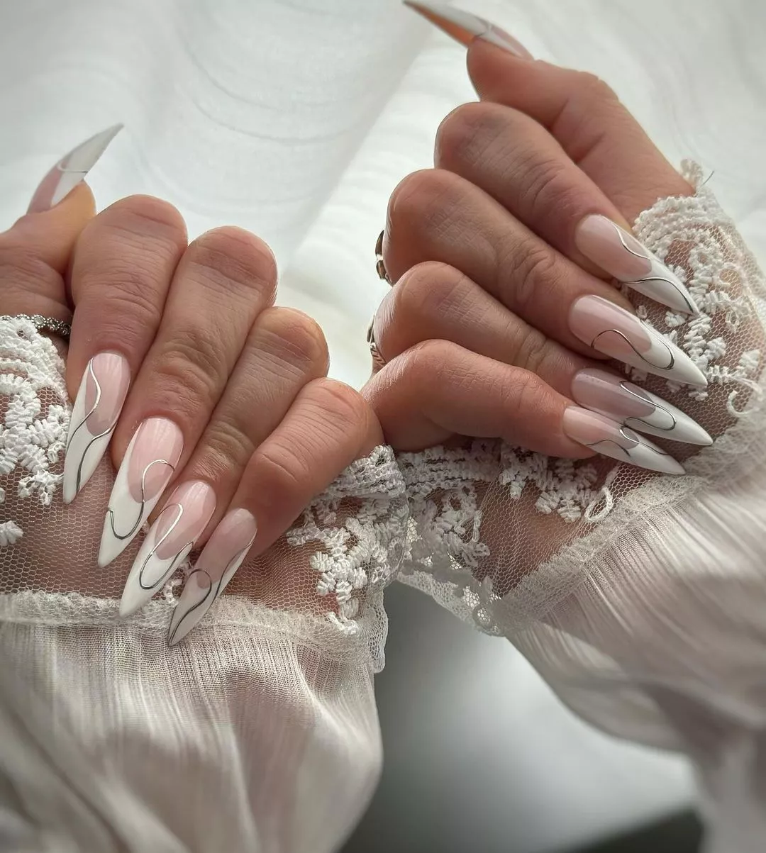 Hands with long manicured nails featuring intricate metallic designs in a closeup view