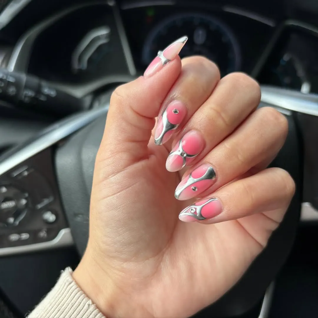 A wellmanicured hand with elaborate nail art featuring pink and metallic silver patterns in a car interior setting