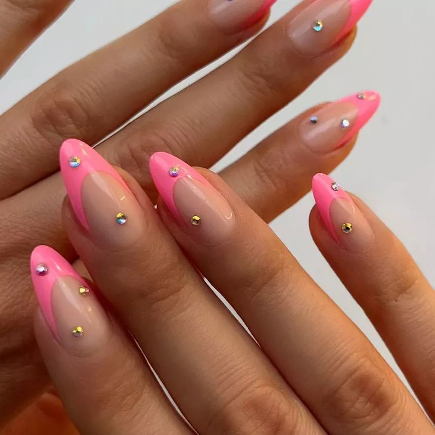 Person shows off their almond-shaped nails with pink French tips and 3D gems