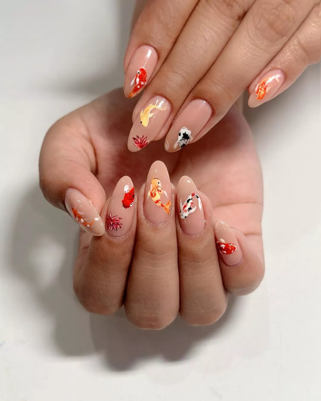 Person shows off their nude base nails with colorful koi fish on each finger