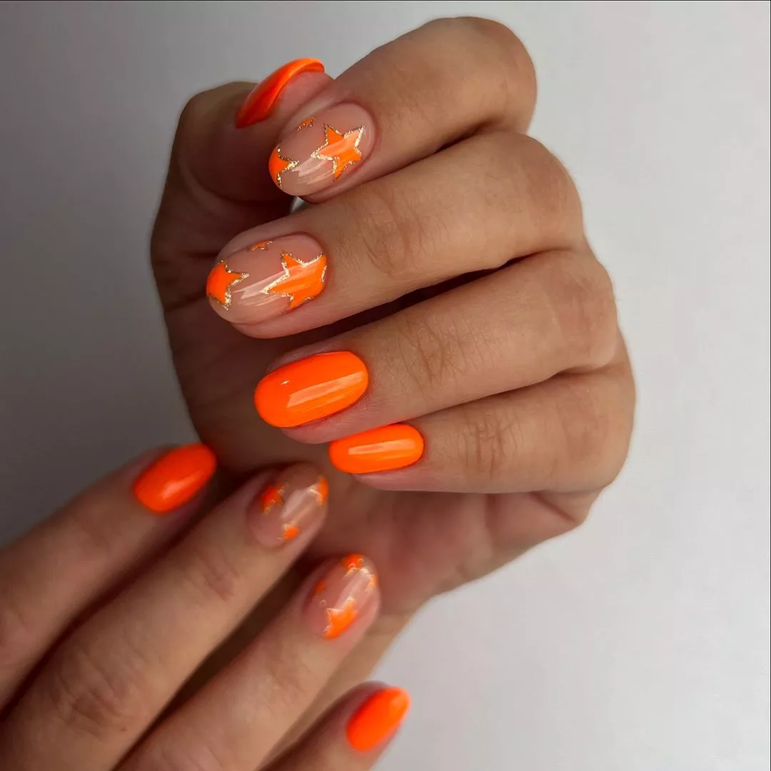 Person shows off their short, oval-shaped nails in neon orange with star accents