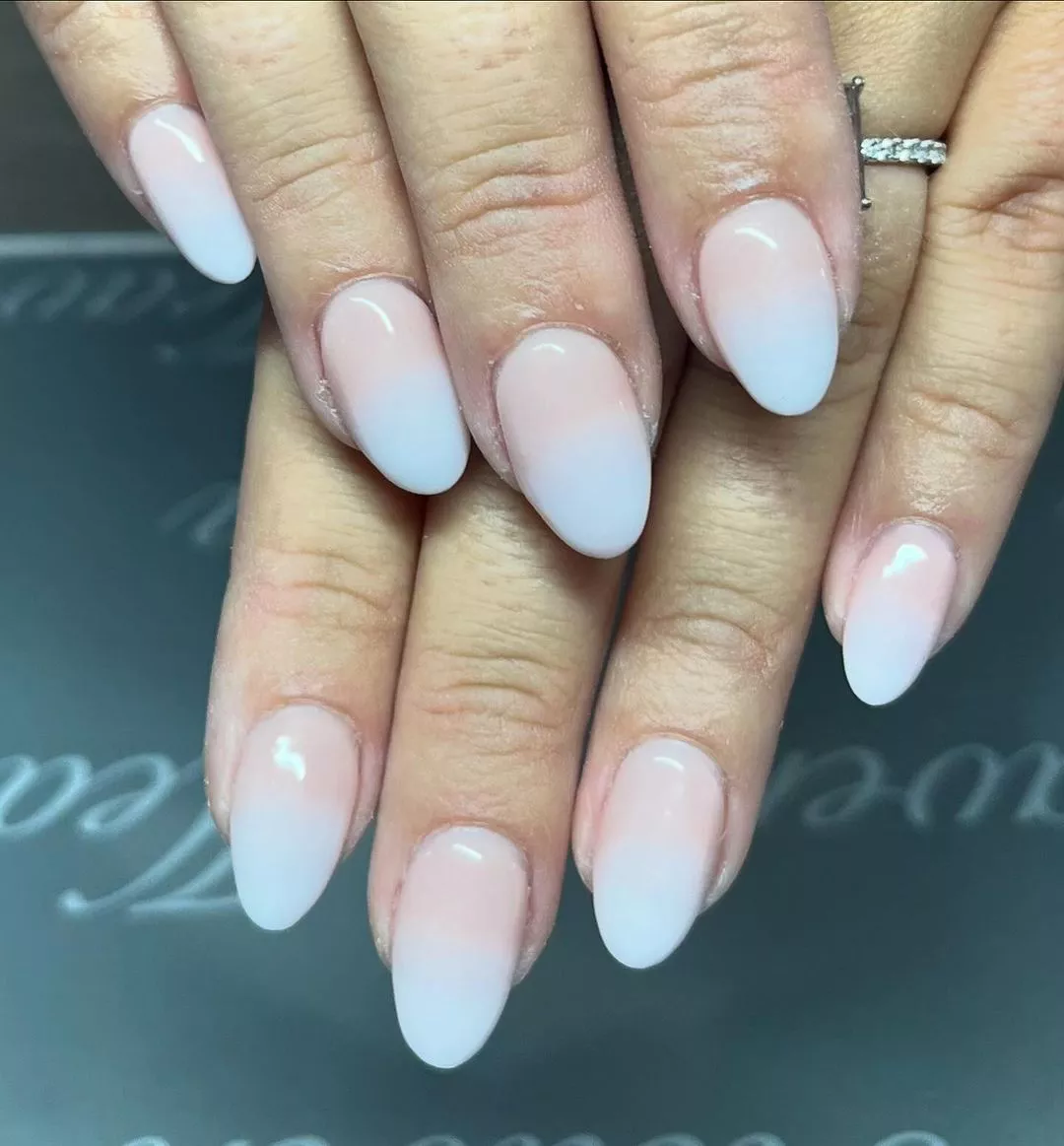 Person with oval-shaped nails in a gradient of light pink at the base and baby blue at the tips