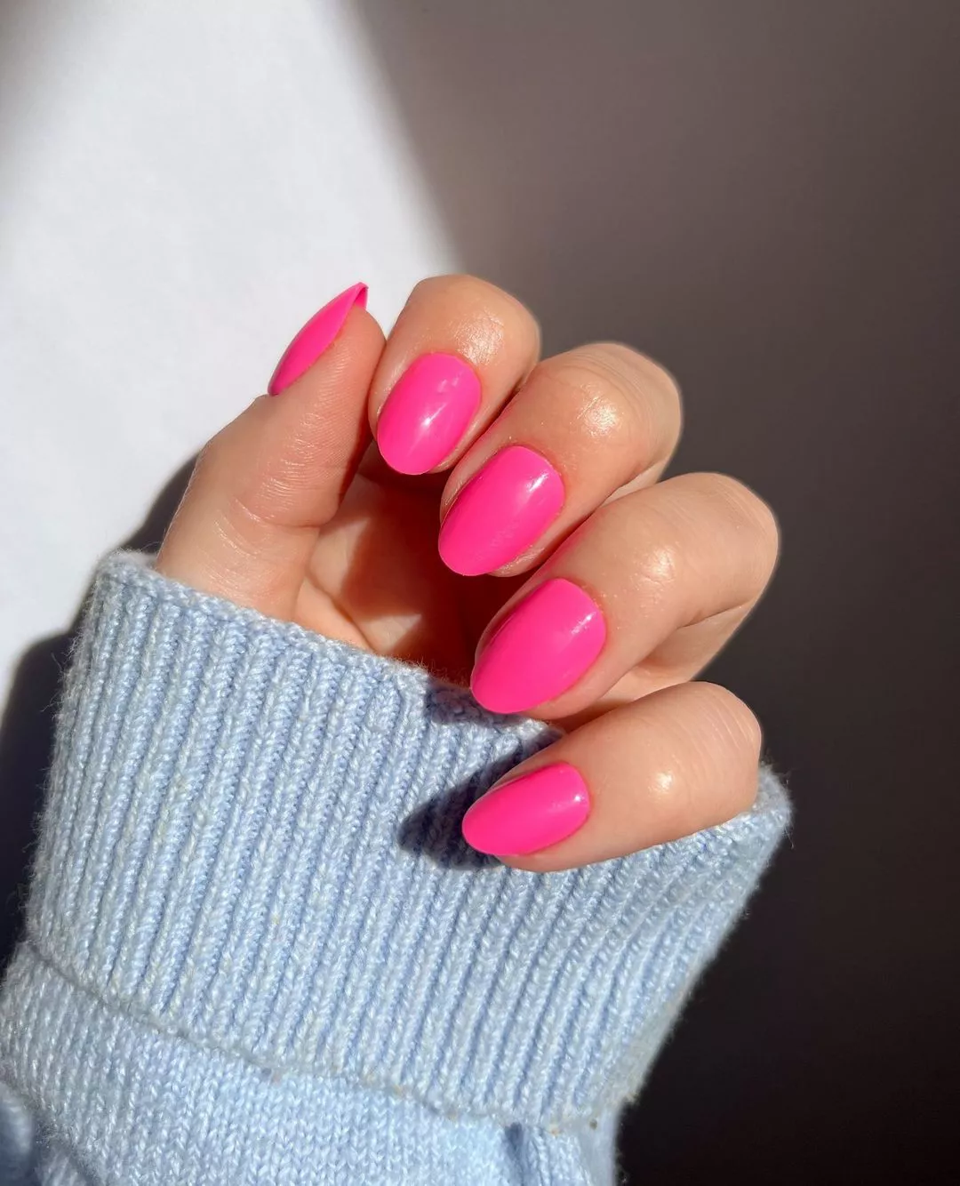 Person shows off their oval-shaped nails, which are painted a solid hot pink
