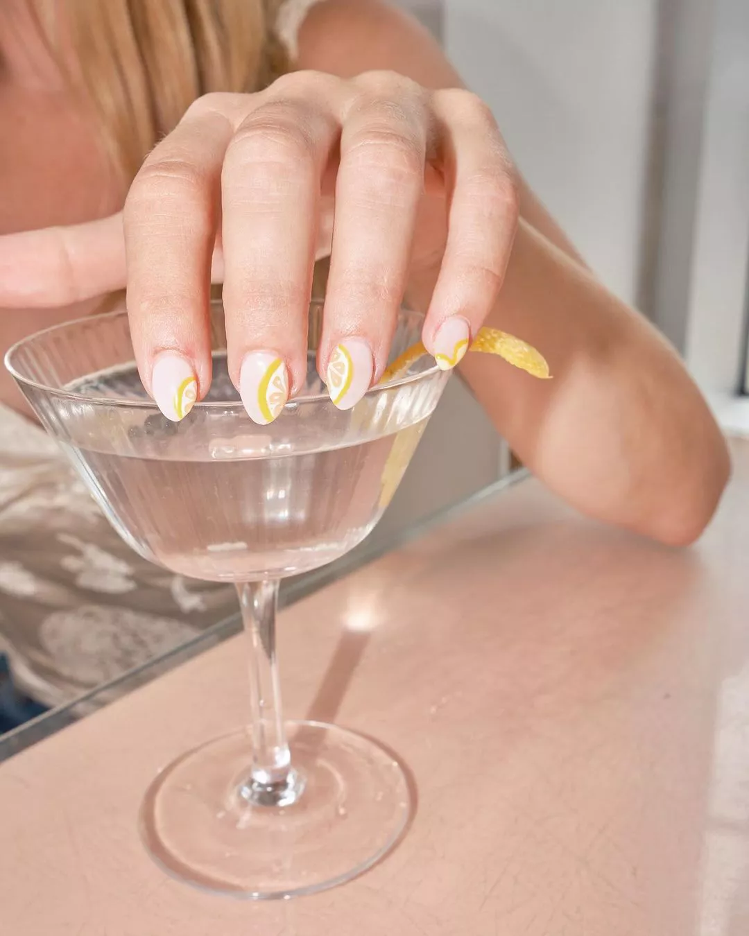 Person shows off their short, oval-shaped nails, which have a sheer base and lemon wedge accents