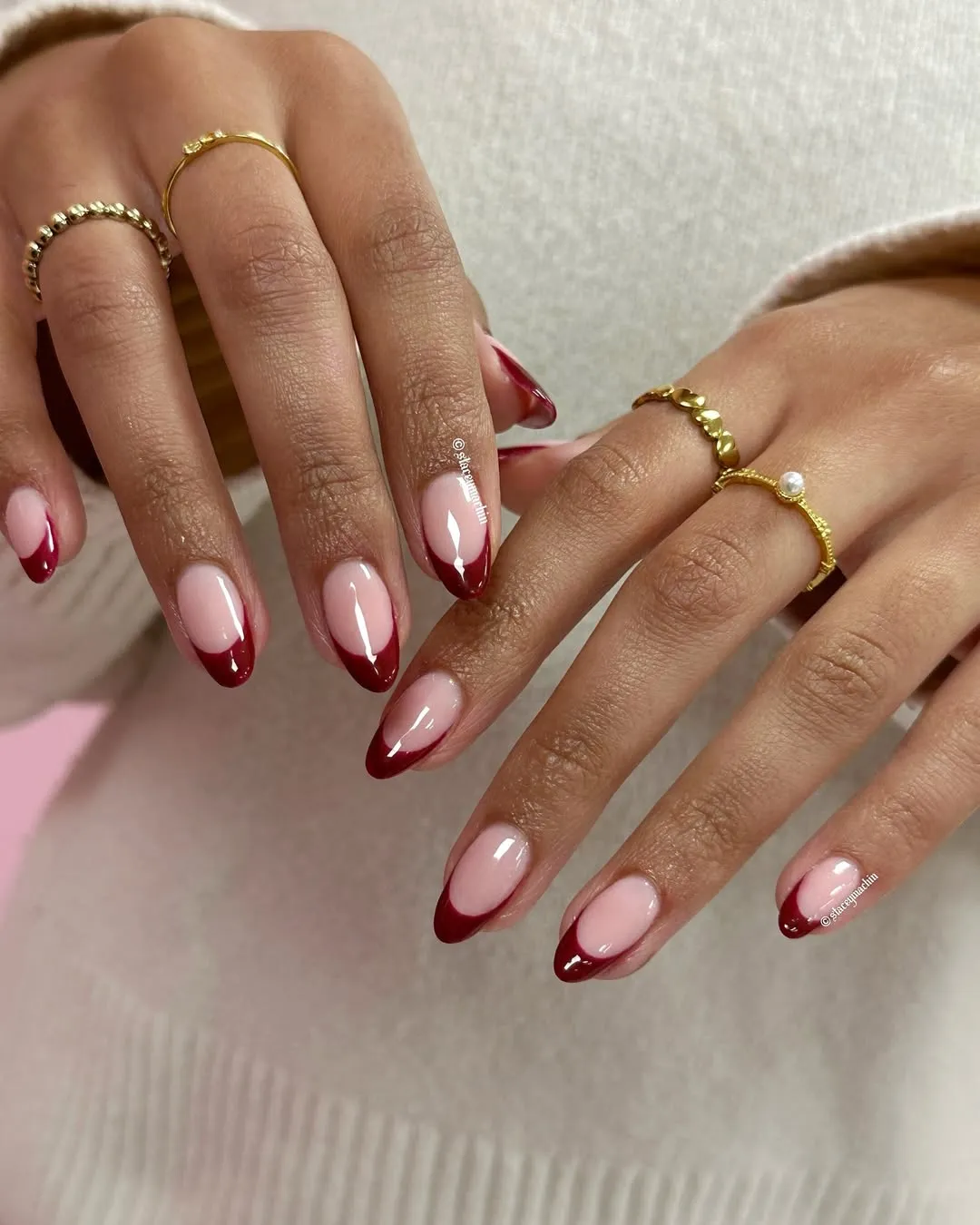 Hands with manicured nails and red tips adorned with gold rings