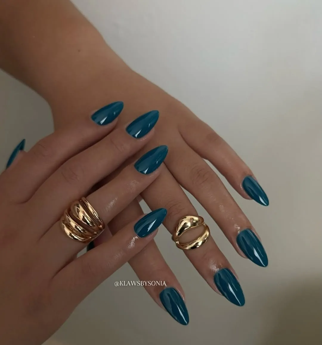 Womans hands with a blue chrome manicure and gold rings