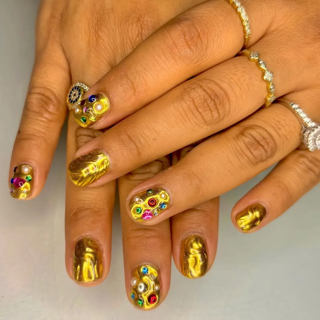 Person with textured gold nails that alternate between solid color and gemstone adorned
